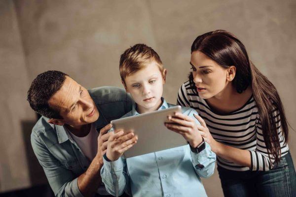 Sorgerecht & Obsorge Vater und Mutter hocken hinter Kind mit Tablet in der Hand